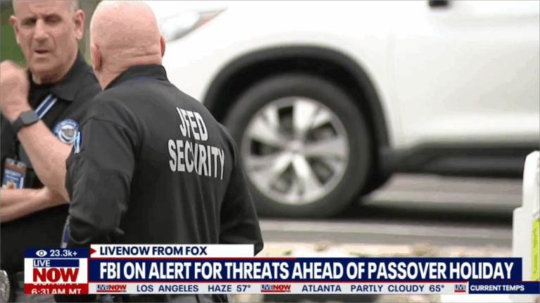 Two security guards, one with his back to the camera wearing a black shirt that says "JFED SECURITY" in white letters, stand near a white SUV. A news banner at the bottom reads "FBI ON ALERT FOR THREATS AHEAD OF PASSOVER HOLIDAY.