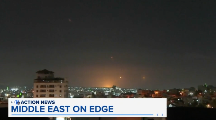 A nighttime cityscape with multiple explosions or flares in the sky. A news graphic at the bottom reads "ACTION NEWS MIDDLE EAST ON EDGE".