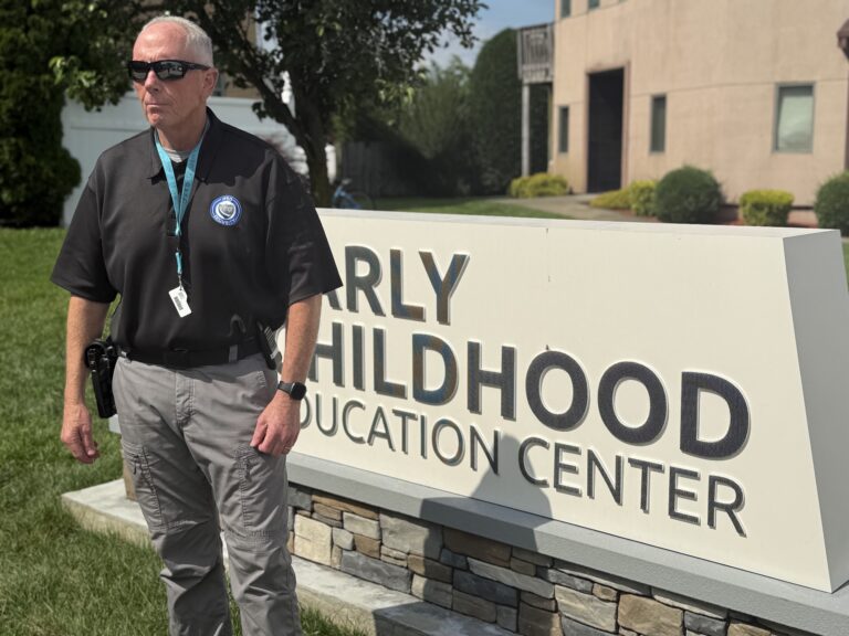 A security guard stands in front of a sign that reads "EARLY CHILDHOOD EDUCATION CENTER".