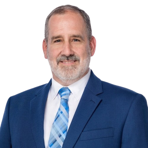 A smiling man with a gray beard and short gray hair wears a blue suit, white shirt, and blue plaid tie.